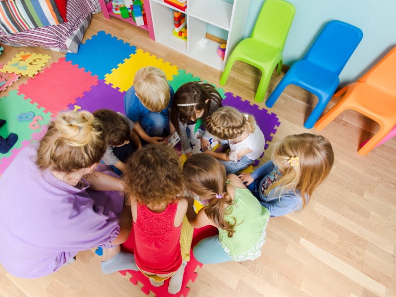 A daycare group activity promotes a child's social skills through teamwork on a colorful, puzzle floor mat.