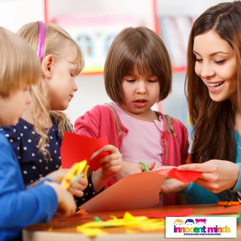 A woman assists children in creating paper crafts, showcasing engaging activities at quality childcare services in Wiley Park