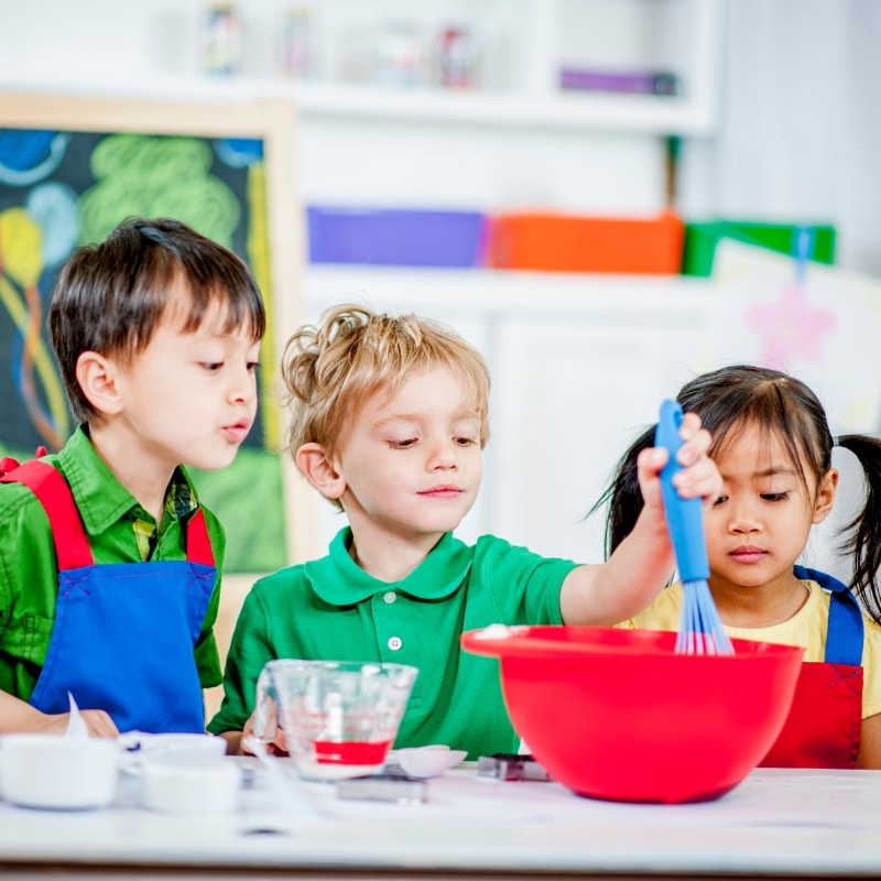 Young children mix ingredients in a bowl during a hands-on activity at a vibrant long daycare centre.