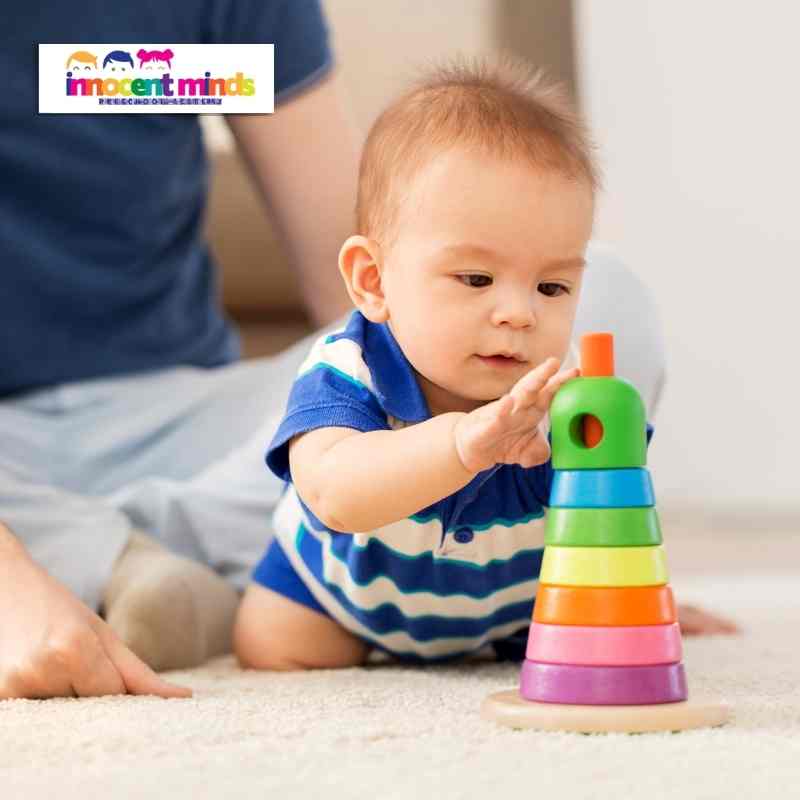 a baby stacking rainbow-coloured rings, developing cognitive skills in a nurturing childcare setting.