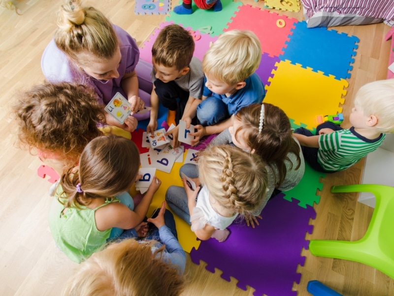 Children receiving help with childcare during a learning activity on colourful mats in a daycare setting.