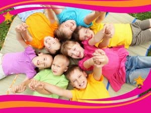 Group of kids lying in a circle outdoors, smiling and holding hands, showing the joy of teamwork games for kids.