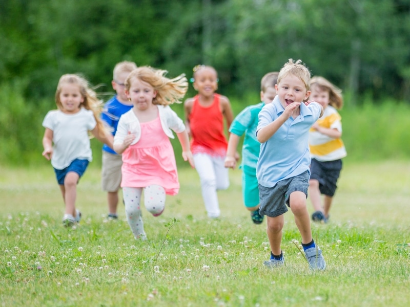 Group of children playing outdoors, demonstrating the benefits of help with childcare through active outdoor play.