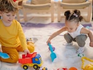 Two young children exploring sand play with toy tools, encouraging smoother daycare transitions through creative activities.