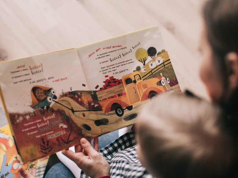 Parent reading a vibrant storybook to a child, showcasing language-building activities for infants.