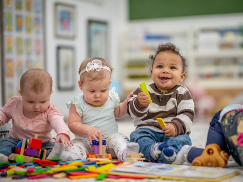 Infants enjoying activities for infants with colourful blocks, supporting their development in a daycare setting.