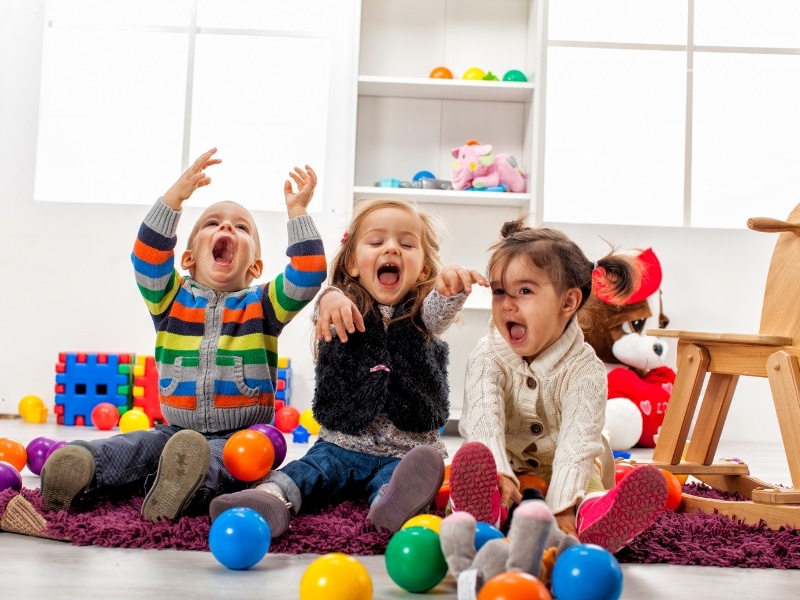 Three toddlers playing with colourful balls in a daycare setting, showcasing joyful daycare transitions.