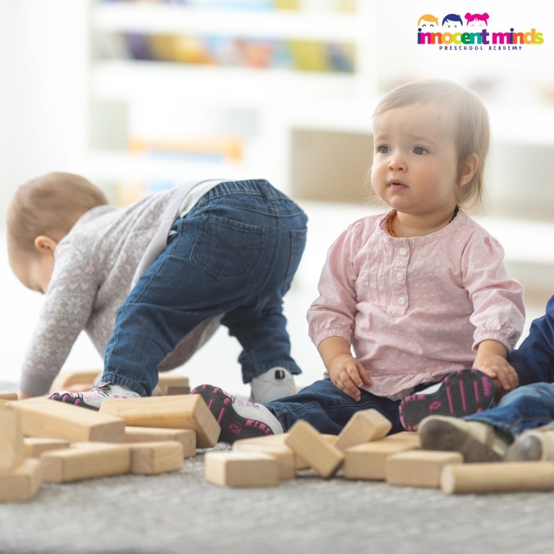 Three toddlers playing with wooden blocks, enhancing their motor skills and creativity through successful program planning for infants and toddlers.