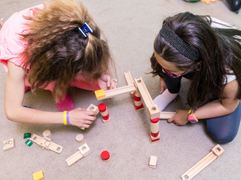 Two girls engaging in cognitive activities for preschoolers, building with wooden blocks