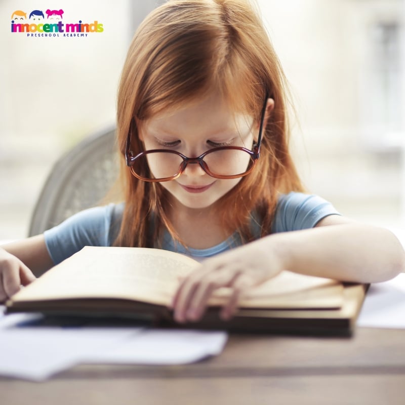 Young girl with glasses reading a book, focused on learning Arabic for kids through engaging study materials.