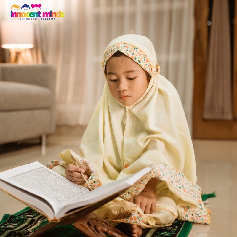 Young girl in hijab reading the Quran with a wooden stand at home – Quran Classes for Kids for early learning.