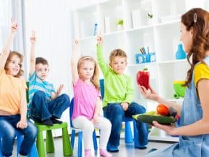 Children participating in toddler programs daily routine with a teacher holding fruits in a classroom