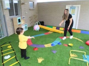 Toddler care activity with child and caregiver playing with ball in vibrant outdoor learning space.