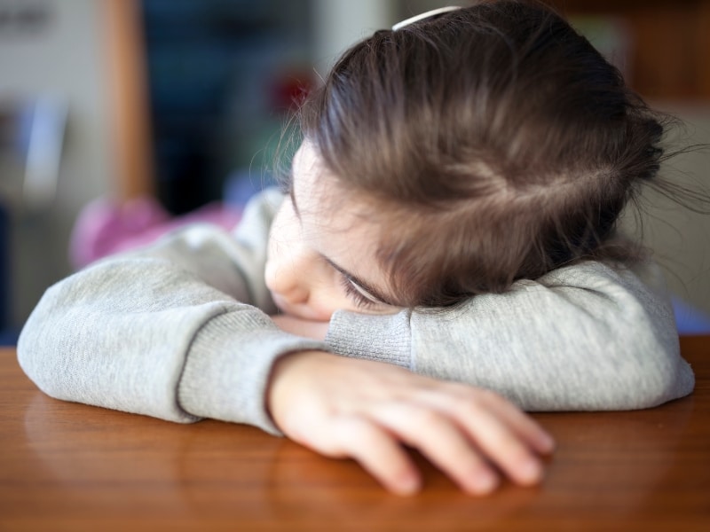 Child resting head on table, illustrating emotional fatigue linked to lack of preschool readiness activities at home.