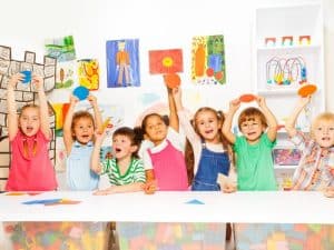 Happy children in a colourful classroom holding up paper shapes, showcasing activities from the best preschool program.