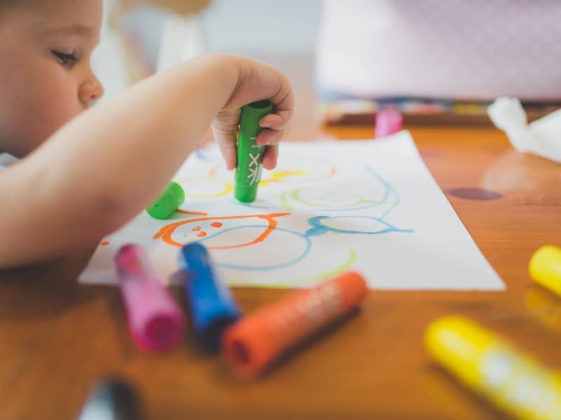 Toddler using vibrant markers for drawing creative preschool readiness activities encouraging coordination and self-expression.